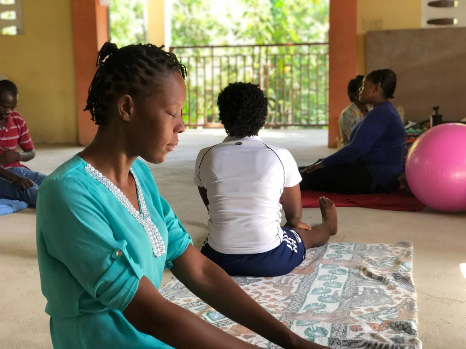 Participants in a group counseling session sit on mats with eyes closed in a calm, open-air room